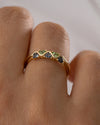 Gold ring with green and blue gemstones on a finger against a neutral background