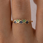 Gold ring with green and blue gemstones on a person's finger closeup