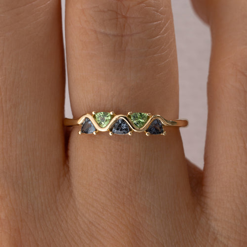 Gold ring with green and blue gemstones on a person's finger closeup