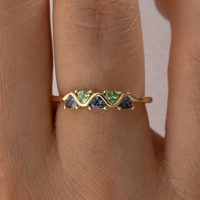 Gold ring with green and blue gemstones on a person's finger closeup
