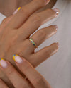 Close-up of a hand wearing a gold ring with colorful gemstones on a neutral background