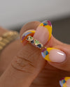 Close-up of a hand holding a gold ring with gemstones against a neutral background