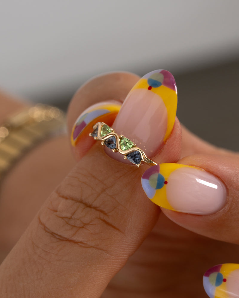 Close-up of a hand holding a gold ring with gemstones against a neutral background