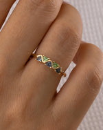 Gold ring with green gemstones on a hand against a neutral background