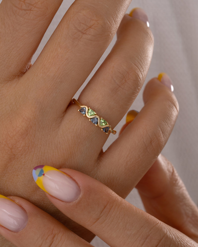 Close-up of a hand wearing a gold ring with green gemstones against a neutral background