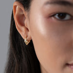 Close-up of a person wearing a gold earring with a neutral background