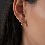 Gold earring worn by a person with dark hair on a dark grey background
