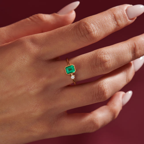 Emerald-Engagement-Ring-with-A-Small-Diamond-symmetric-Emerald-Ring-on-finger