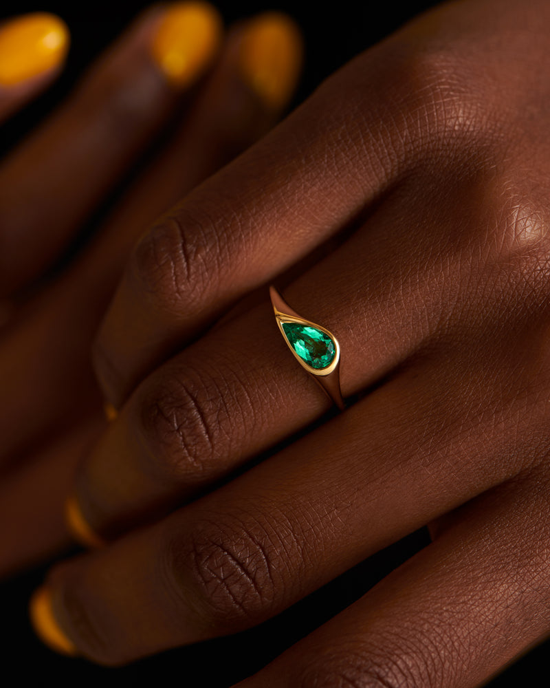 Solitaire-Engagement-Ring-with-a-Pear-Cut-Emerald-on-finger